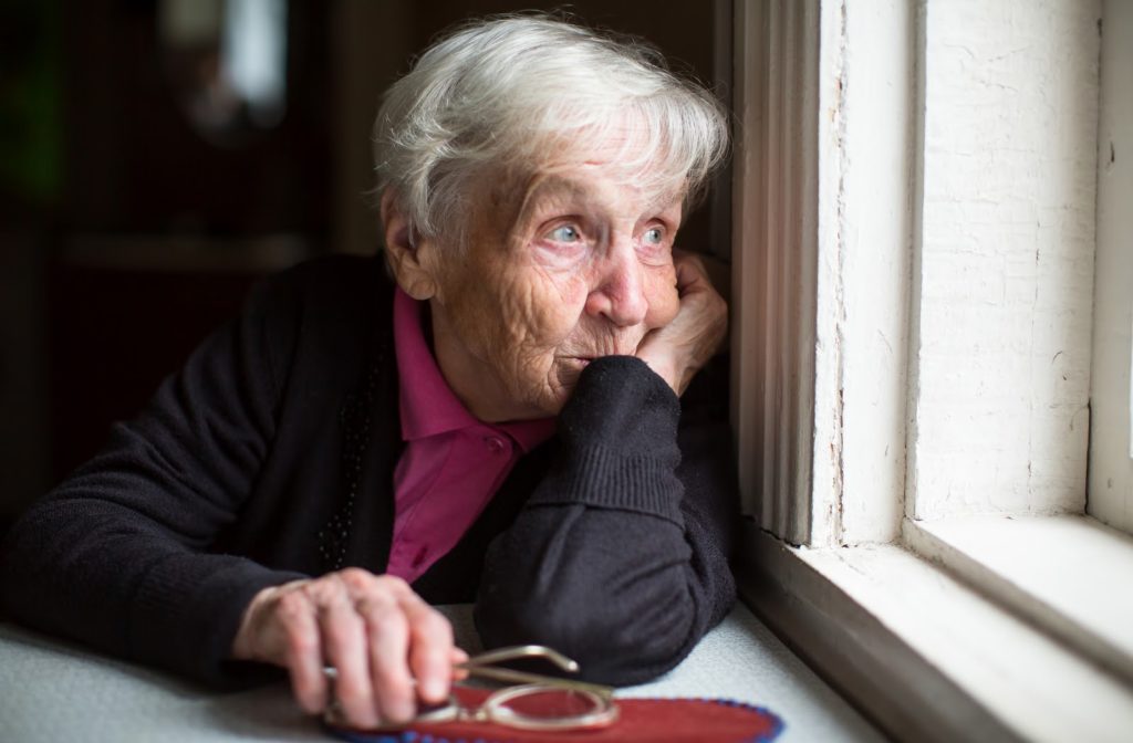 Sad senior women looks out window as she leans against it