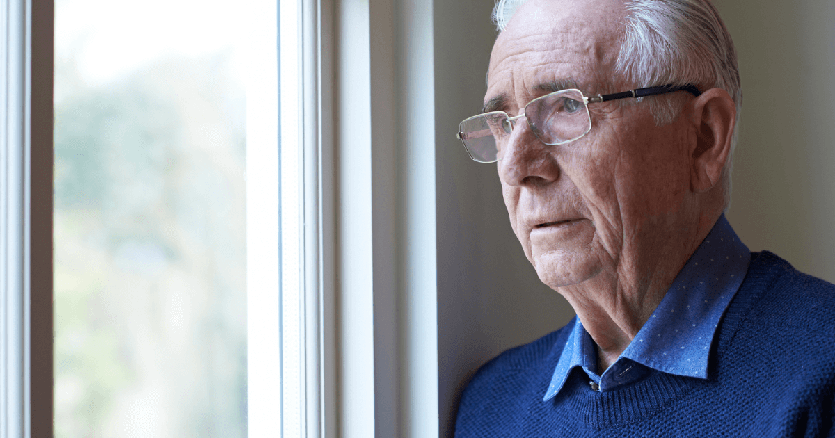 Senior man gazing out of the window thinking about stages of dementia