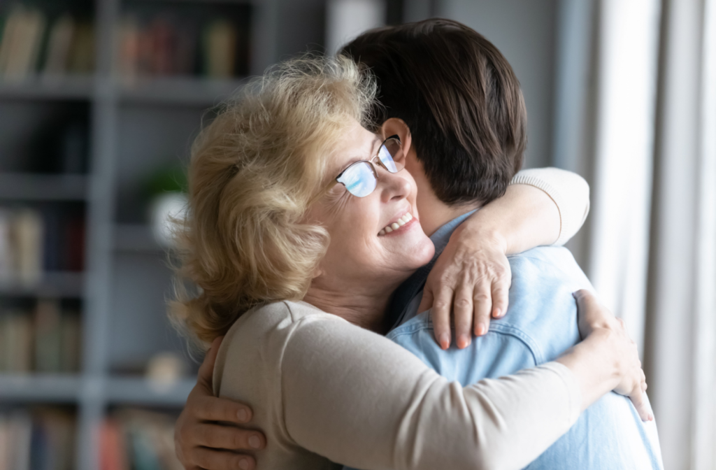 A senior parent tightly hugs their adult-child with a joyful expression on their face.