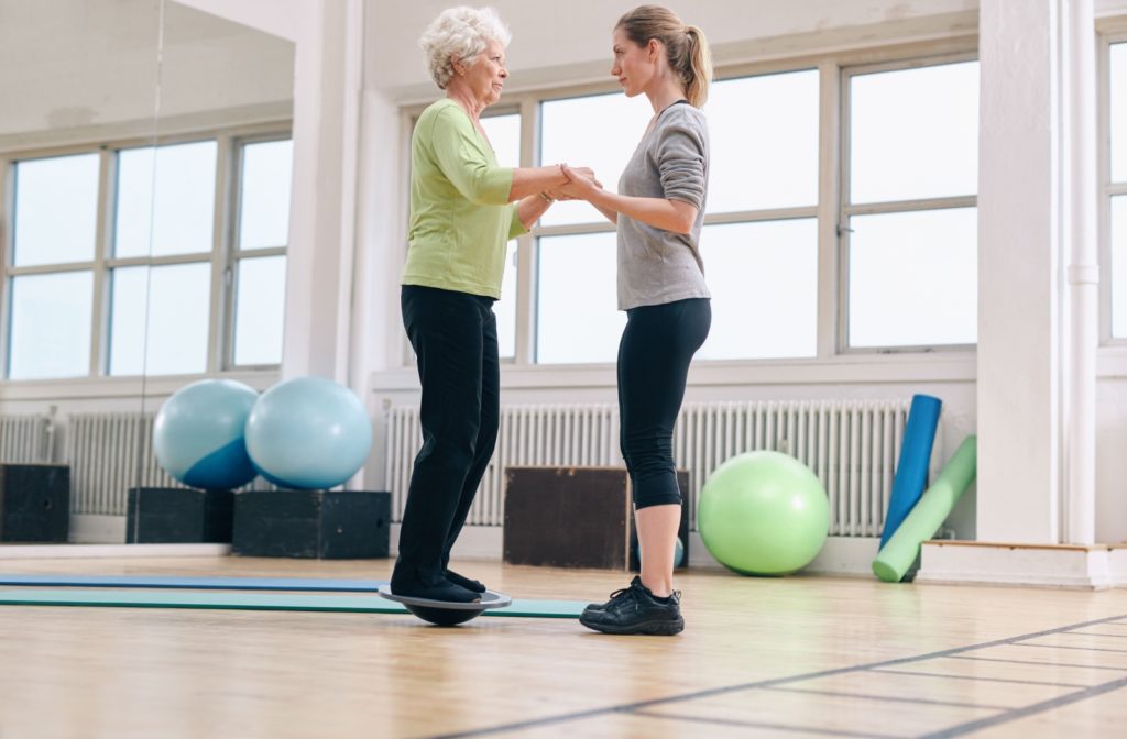 A personal trainer helping support an older adult while performing a balance exercise.