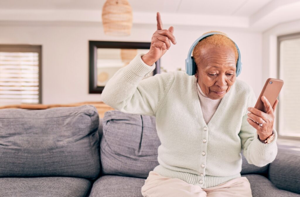 A senior wearing blue headphones uses their phone to connect to a music app like Spotify to hear music from their childhood