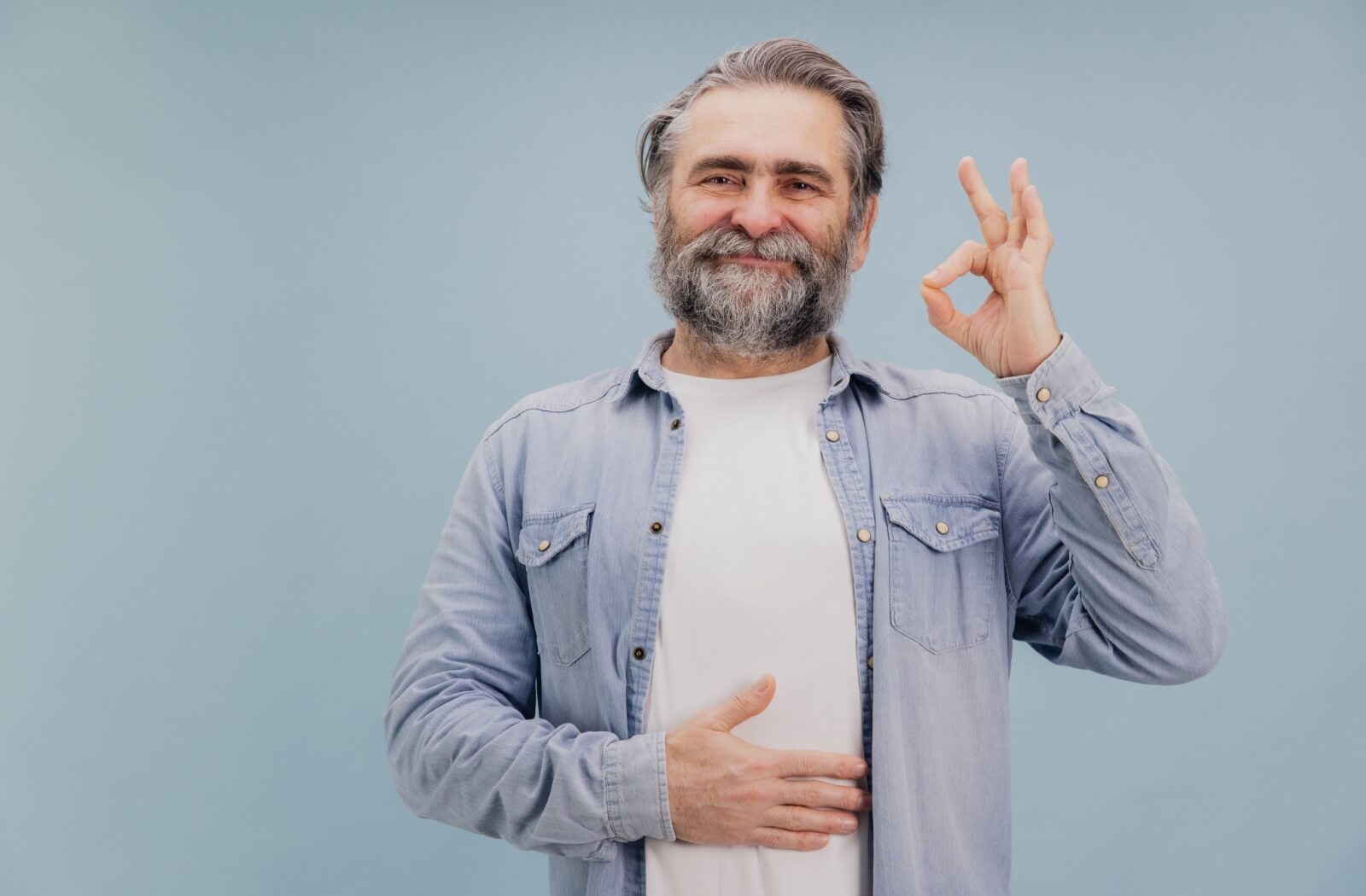 A senior holds their hand to their stomach, and their other hand in an OK sign, representing feeling good about gut health