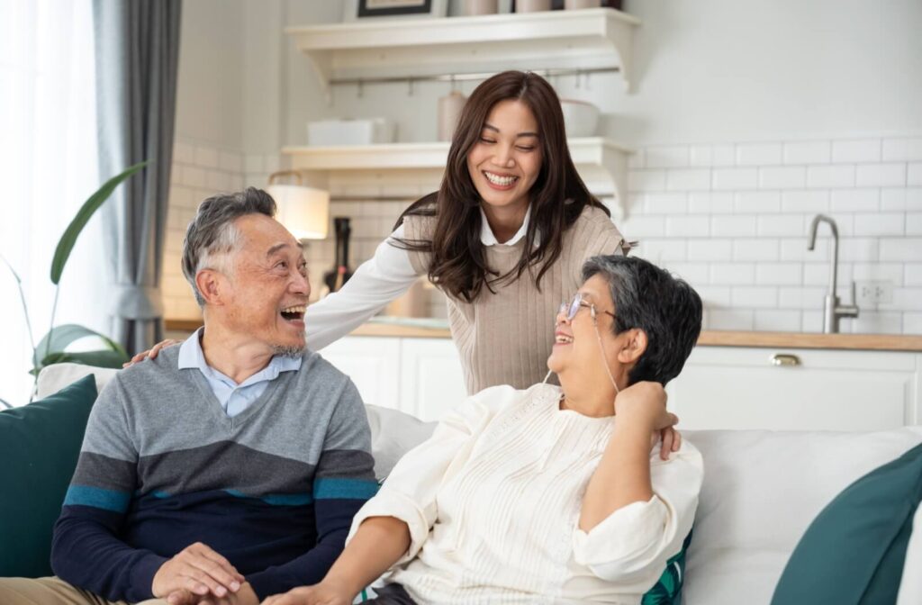 An adult smiles and laughs with their senior parents during a visit to their assisted living home