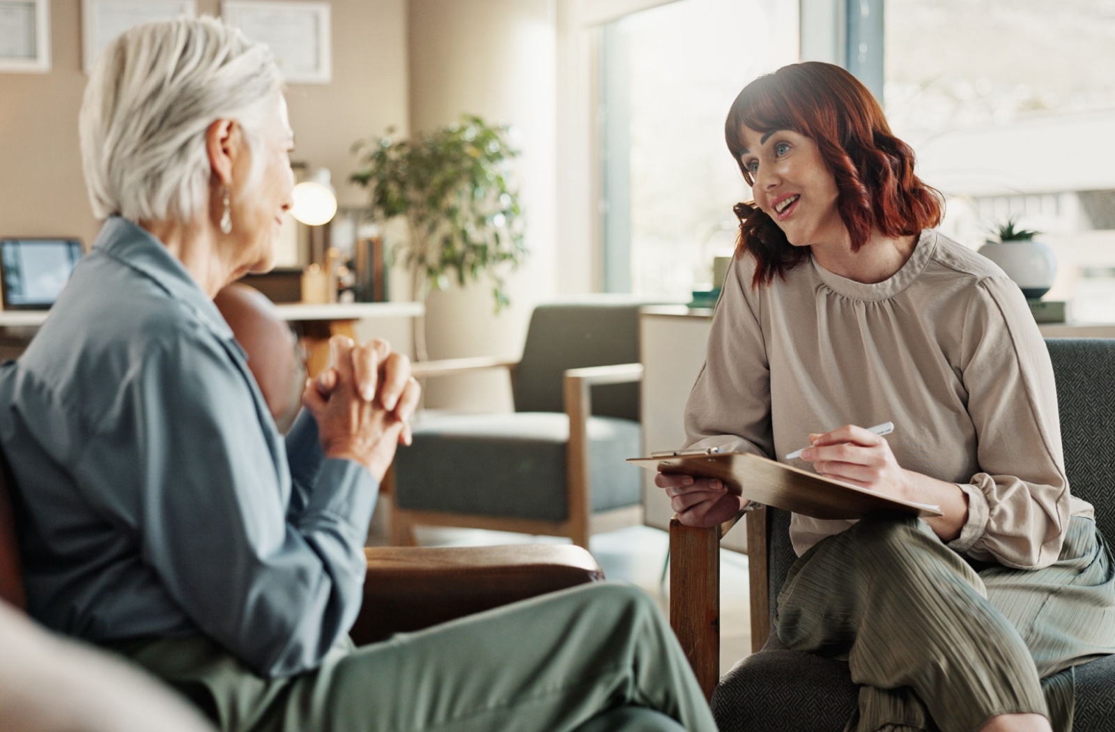 An older adult sitting in a cozy office and talking to a geriatric care manager as they take notes.