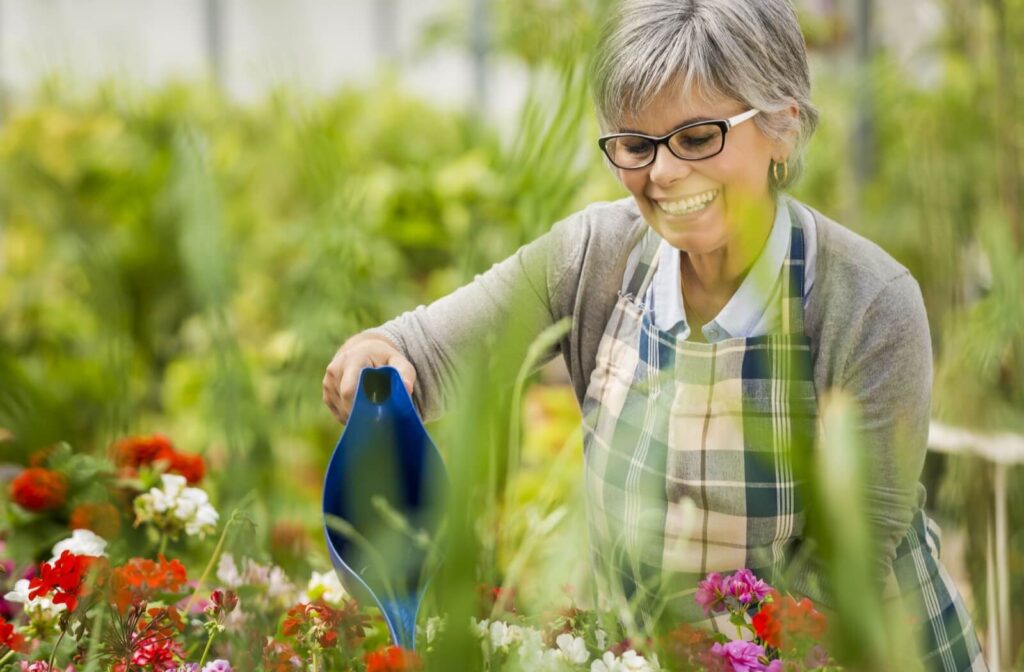 A senior with dementia smiles as they water flowers in the outdoor garden of their memory care home as part of their routine